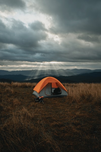 在多云的天空下，在棕色的田野上搭起灰色和橙色的帐篷